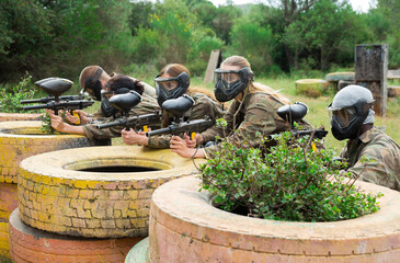 Group of young paintball players aiming with guns in shootout outdoors
