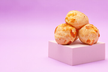 A pile of cheese breads on a podium, Brazilian traditional Pao de Queijo, on pink background