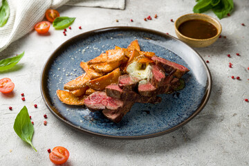 Beef steak sliced with potato wedges on grey table