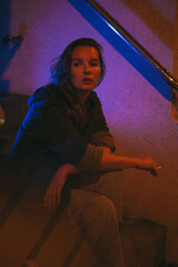 Girl with a cigarette at night sits against the background of neon light