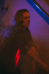 Girl with a cigarette at night sits against the background of neon light