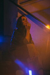 Girl with a cigarette at night sits against the background of neon light