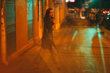 A girl walks around the city at night after the rain among the light of lanterns and cars