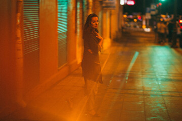 A girl walks around the city at night after the rain among the light of lanterns and cars