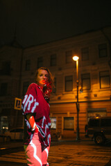 A girl walks around the city at night after the rain among the light of lanterns and cars