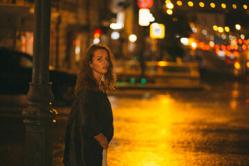 A girl walks around the city at night after the rain among the light of lanterns and cars
