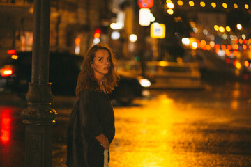 A girl walks around the city at night after the rain among the light of lanterns and cars