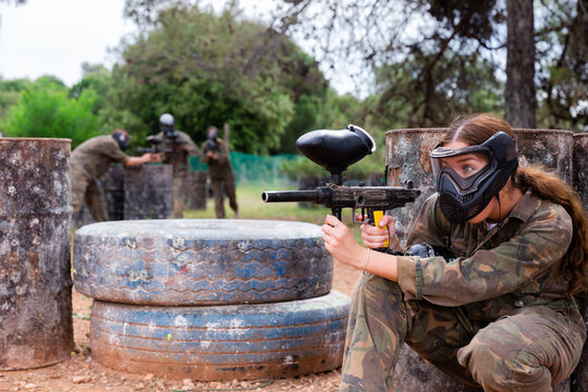 Paintball players of one team in camouflages and masks aiming with gun in shootout playing field