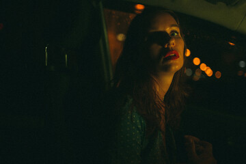 A girl sits in a car at night with red lips against the backdrop of city lights