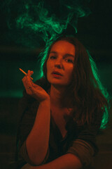 Girl with a cigarette sits at night against the background of red and green light