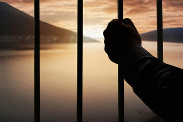 Silhouette of a man's hand in a prison behind a steel cage holding a cage. with natural mountain...