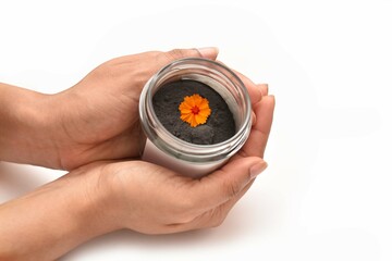 A girl Holding a bottle of cosmetic with an orange colour flower. The scrub is made out of charcoal and carbon. 