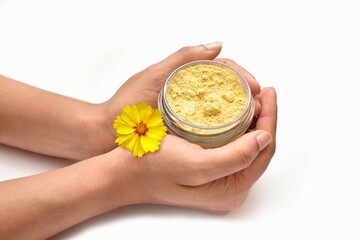 A girl Holding a bottle of cosmetic with a yellow flower. The scrub is made out of  Turmeric .
