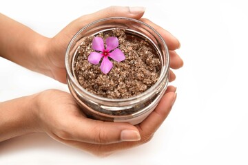 A girl Holding a bottle of cosmetic with a pink flower. The scrub is made out of  brown sugar.