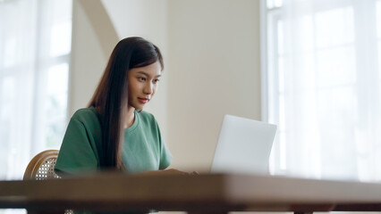 Young asian woman working at home. Female using computer laptop on desk at house