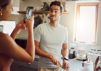 Silly, goofy and interracial couple taking pictures, having fun and cooking together in the kitchen at home. Happy girlfriend taking pictures of boyfriend, making funny faces and preparing dinner