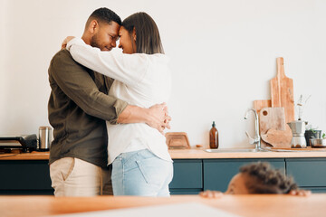 Cosy couple hugging, romance and affection in a modern kitchen with small child looking at them. Loving, young and parents, mom and dad embrace, excited by the future of their growing family