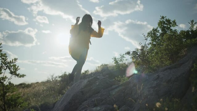 A girl on a dangerous hiking trip in the mountains walks along the rocks to the top. A woman in a yellow jacket climbs the mountains. High quality 4k footage