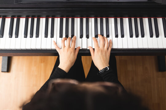 Top view of woman's hands playing piano by reading sheet music. 