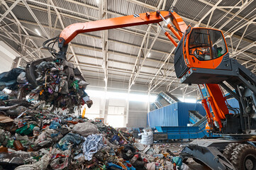 Excavator grabs trash in warehouse of waste processing plant