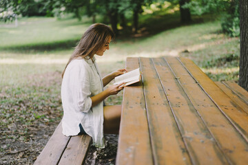 Woman holds book in her hands. Reading the book sitting on a bench at outdoors