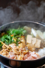 煮込まれ沸騰し湯気の立つ鶏肉のすき焼き鍋