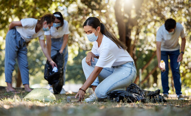 Group of volunteers picking up, cleaning and reducing pollution in a public nature park together. Diverse community wearing face masks to protect from disease, collecting dirt and doing cleanup