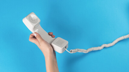 The left hand of a girl with a telephone receiver with a wire on a blue background.