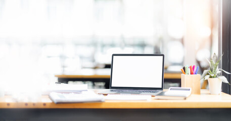 Laptop screen, computer, notebook, workspace and eyeglasses sitting on a desk in a large open plan office space after working hours	