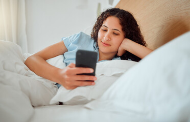 Woman texting, checking messages and holding phone while reading sms and lying awake in her bed in the morning. Happy, content and smiling female playing a game, browsing the internet or social media