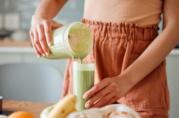 Woman pouring healthy smoothie in a glass from a blender jar on a counter for detox. Female making...