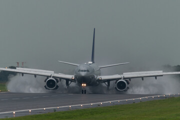 avion de pasajeros aterrizando en un dia lluvioso, con pista mojada. avion desplegando reversores y levantando spray, con cielo gris - obrazy, fototapety, plakaty