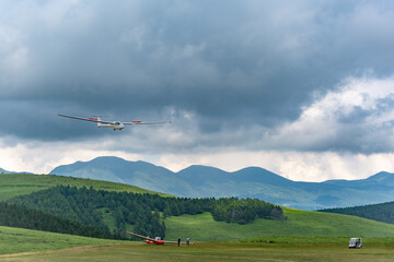 Fototapeta na wymiar 暗雲と山並みを背景に高地の滑空場に着陸するグライダー。自然,環境,レジャーのイメージ