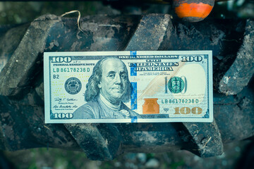 One hundred US dollar banknote lies on the tread of a tractor wheel close-up top view. Paper money...