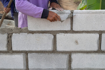 Constructor hand holding a plastering trowel and concrete block to build a fence for a country house.