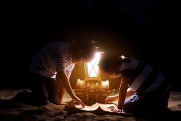Children dressed as sailors play on the sand at night by the light of a lantern and imagine themselves as pirates looking for treasures on the map. Funny kids dream of adventure and travel. - 524174956