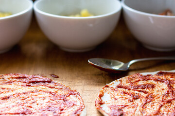Two pizza bases with additional ingredients in white bowls