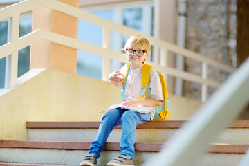 Smart little child sitting and reading on the stairs of school building. Quality education for...