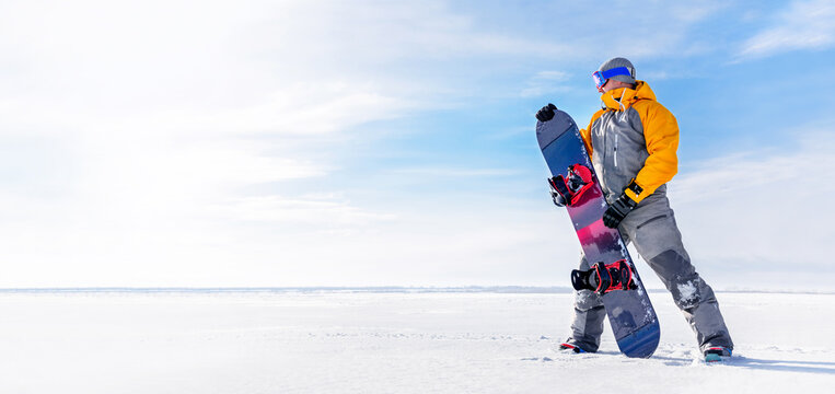 Young man holds a snowboard in his hands against the background of a winter landscape.