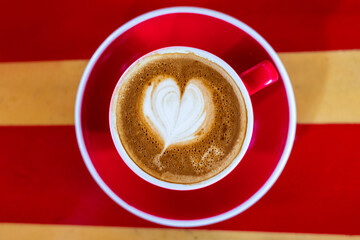 milk love heart on a flat white coffee in a red and white cup