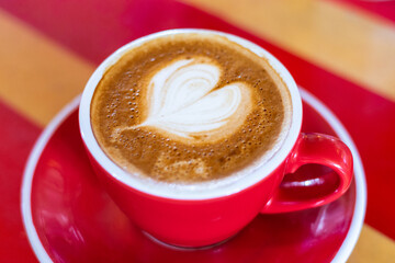milk love heart on a flat white coffee in a red and white cup