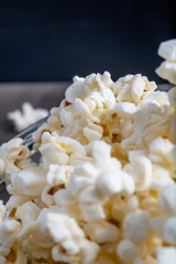 Vertical close-up photo of a set of popcorns inside a glass bowl, image of various popcorn inside the bowl with a black background.