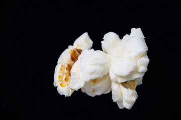 Close Up photo of just one white fluffy popcorn on a black background, an image of an isolated popcorn.