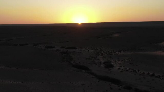 Backlit panoramic aerial drone sideways view of Martian Erfoud desert landscape in Morocco at sunset or sunrise