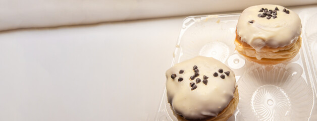 Two delicious donuts with icing sugar and chocolate chips on a white background in a plastic transparent container, a banner with a copy of the space on the left