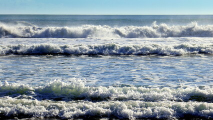 Meeresstrand mit sich brechenden Wellen und blauem Himmel am Horizont