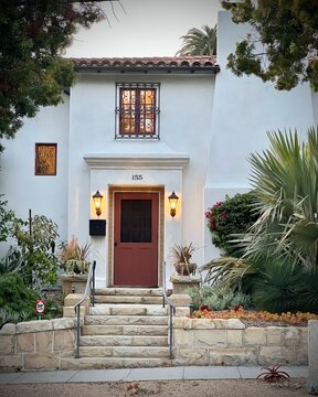 a santa barbara residence.  adobe style home. palm trees with yellow porch lights, picture windows and steps lead to a beautiful door.  architecture digest.