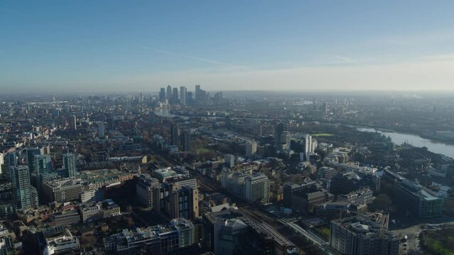 Descending establishing drone shot over the Limehouse district in under a misty blue London sky. The Canary Wharf and the River Thames in the distance.