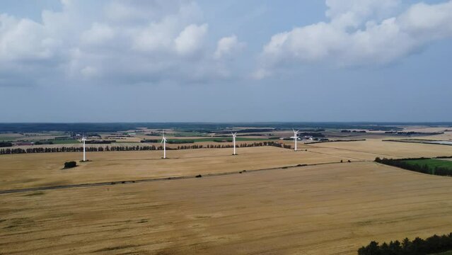 4 wind turbines on a meadow with beautiful clouds in the sky in the background, droneshot