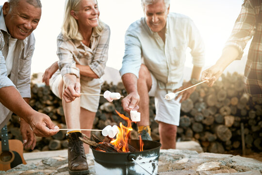 Camping, Hiking And Adventure Senior People Melting Marshmallows In A Camp Fire During A Nature Retreat Or Getaway Outdoors. Happy Retired Or Senior Group Of Friends Enjoying Fun Recreation Activity